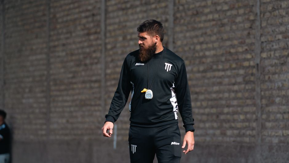 Soccer coach standing outdoors with a stopwatch, dressed in athletic gear.